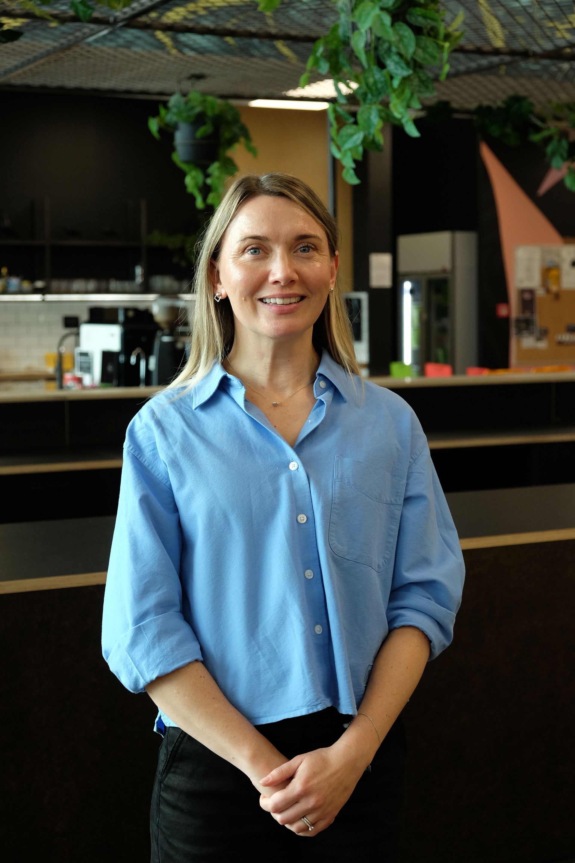 Gina Nicholas  a light blue shirt standing indoors near a counter, smiling at the camera.