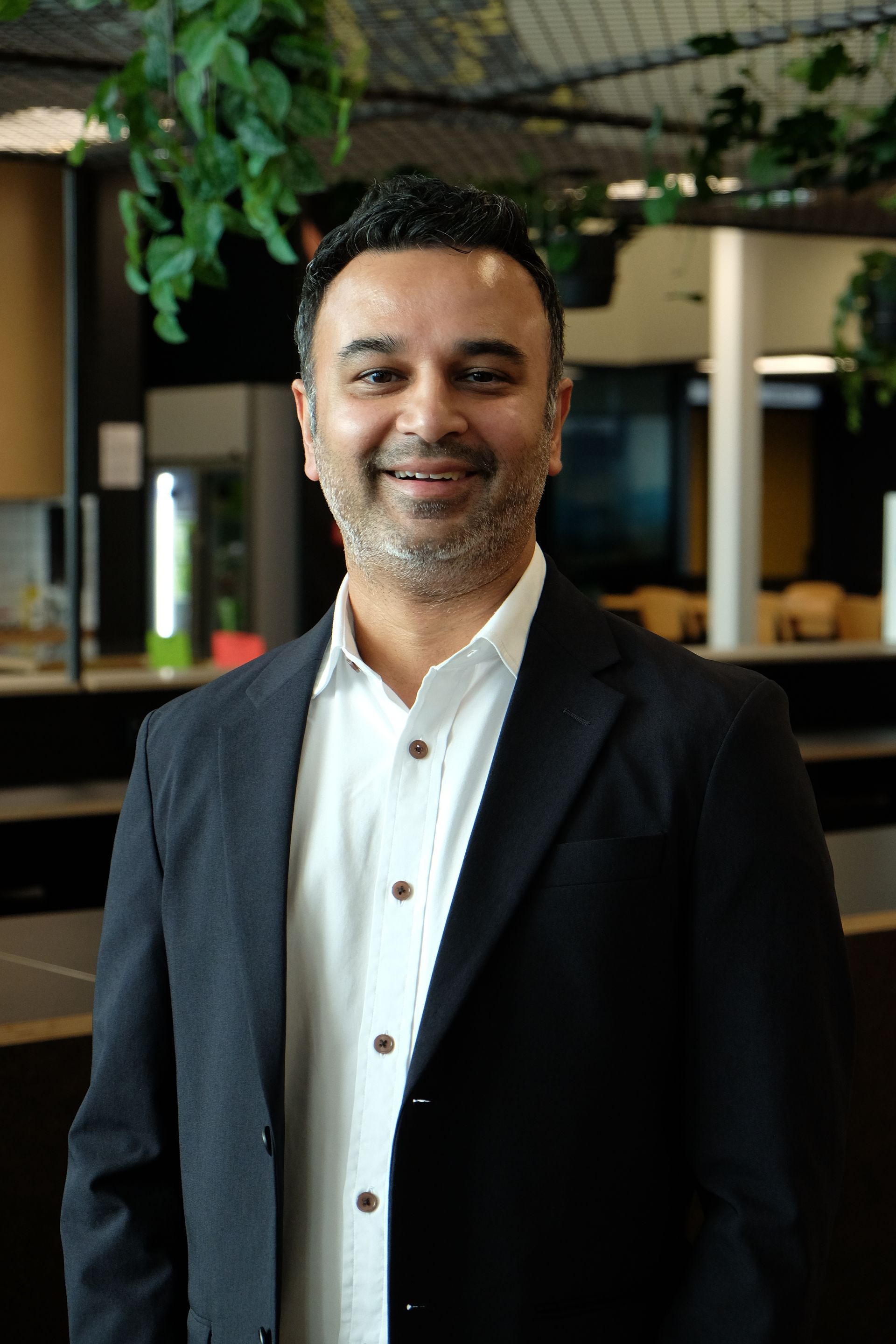Pranil Wadan - Director in a dark blazer and white shirt standing indoors with a modern office background