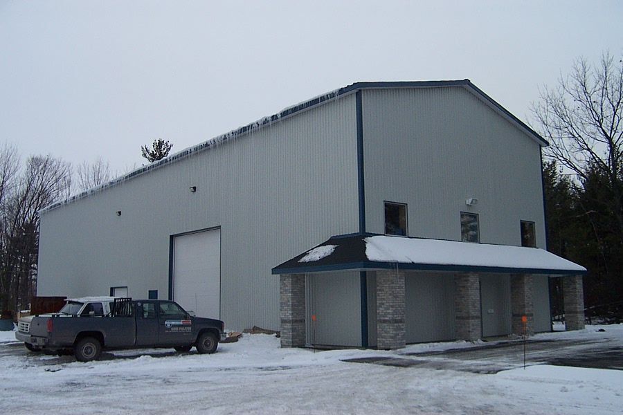 Grand bâtiment industriel gris avec un camion stationné devant, sol enneigé.