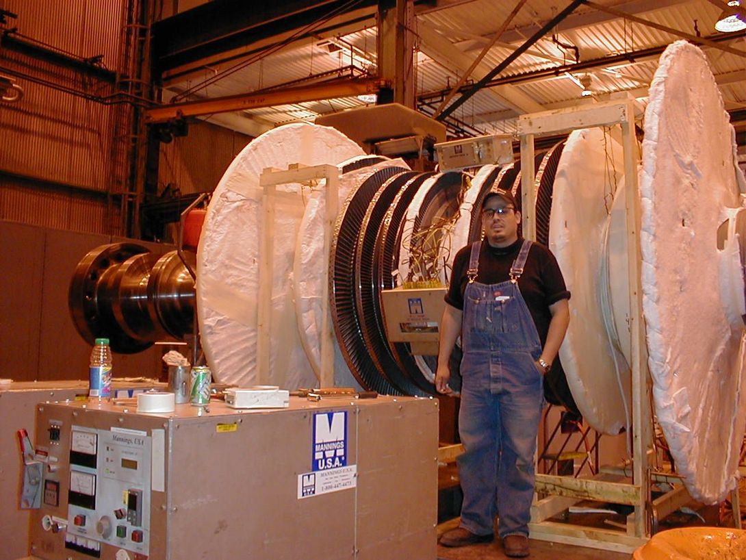 Une personne se tient à côté d’une grande turbine industrielle dans une usine.