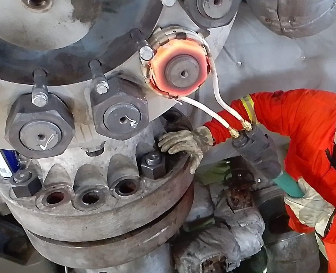 Personne en combinaison de protection orange travaillant sur un équipement industriel, avec un composant chauffant rougeoyant.