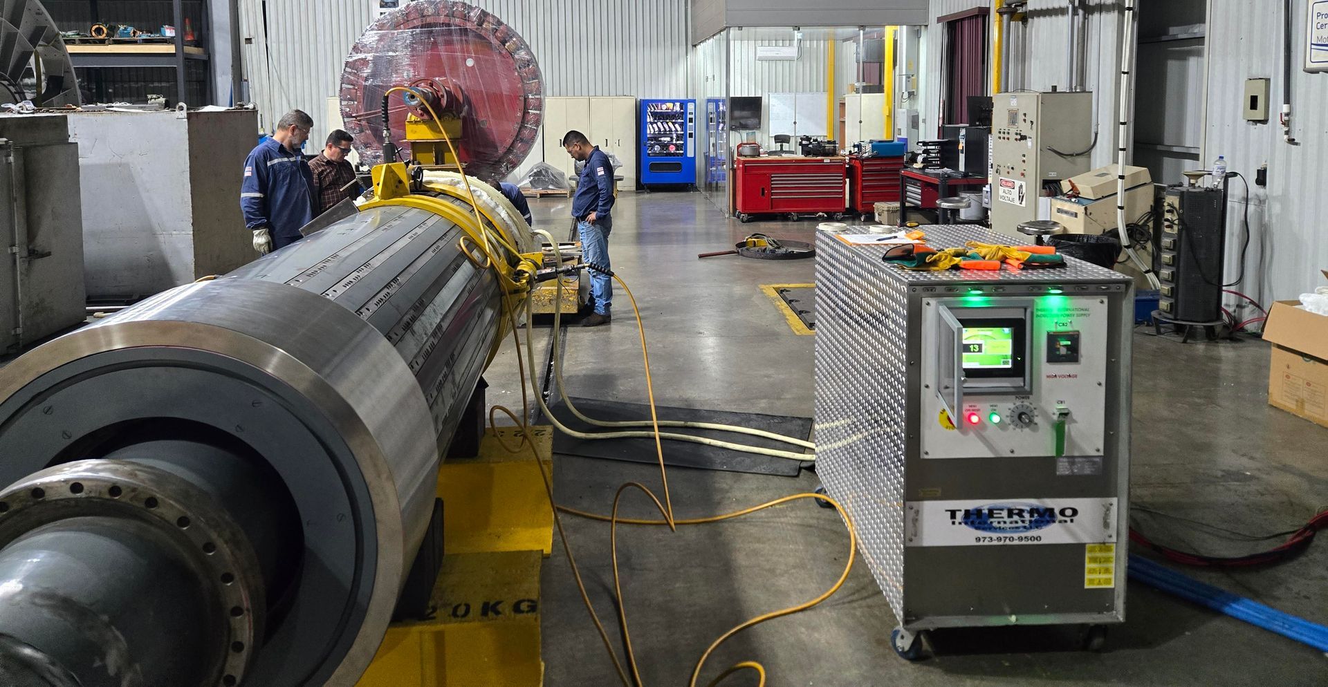Des ouvriers près d'équipements industriels, probablement en train de tester ou de réparer, dans une usine. Le panneau de commande d'une machine est allumé.
