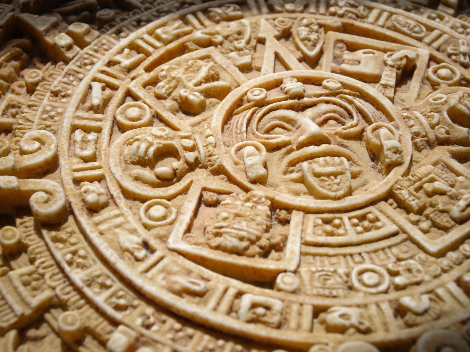 Close-up of a weathered, circular Aztec calendar with carved symbols and a central sun-faced figure.