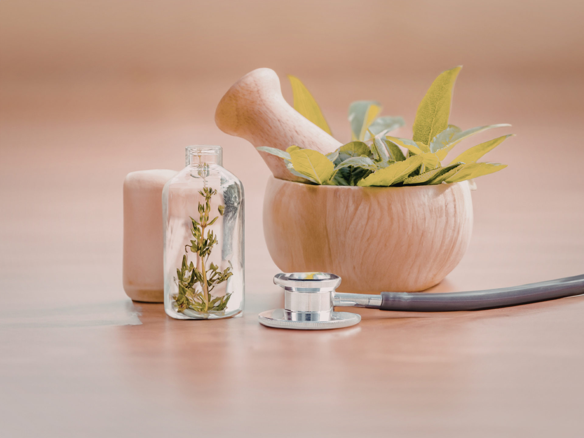 Wooden mortar and pestle with herbs, glass bottle, stethoscope, and soap on wooden surface.