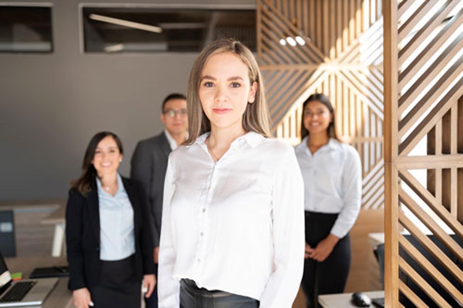 Four professionals in white shirts and black suits standing in a modern office lobby