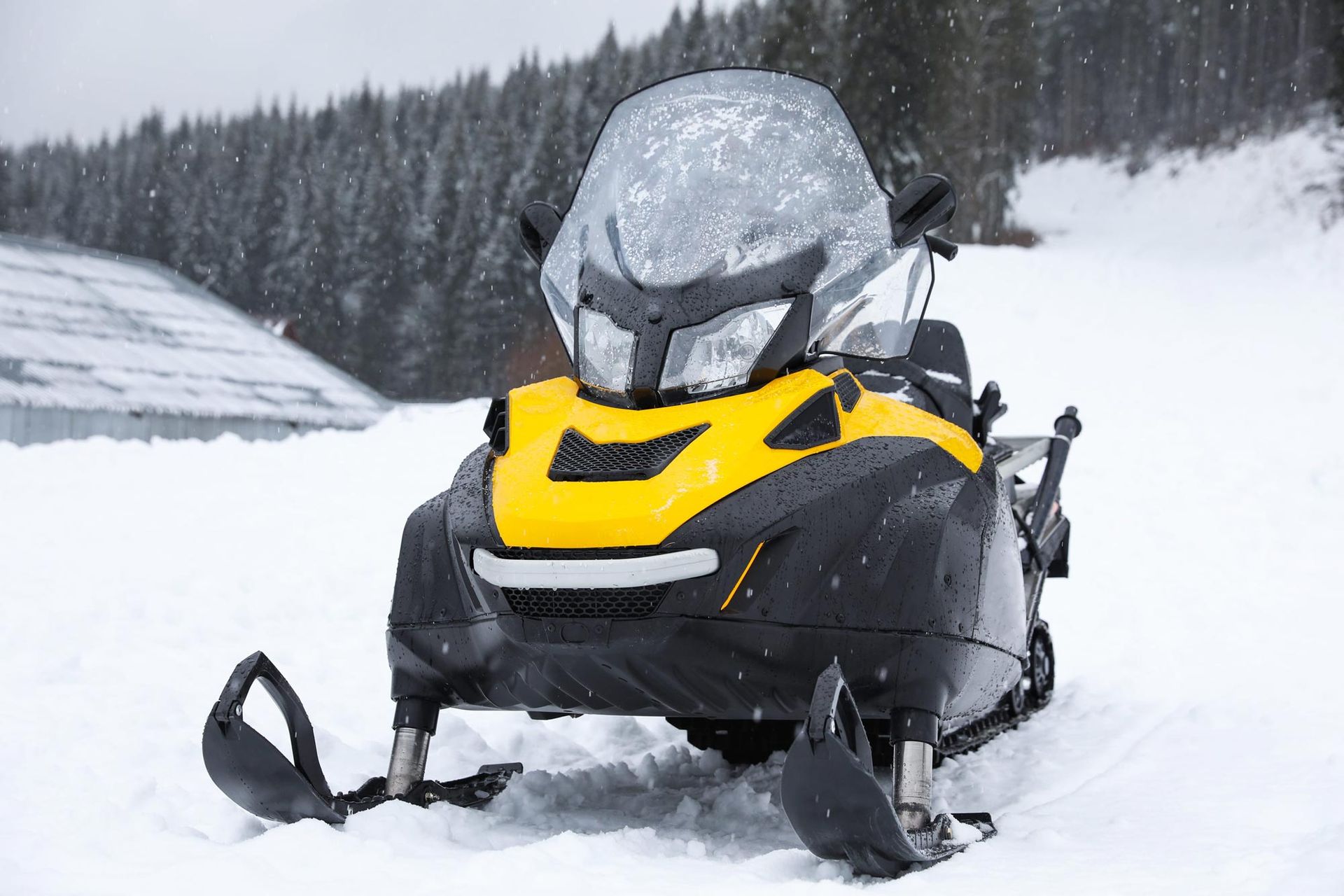 Yellow snowmobile parked in deep snow on a snowy trail beside a forest