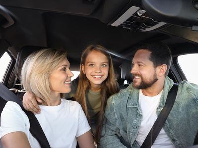 Three people smiling in a car, with the front seats and dashboard visible.