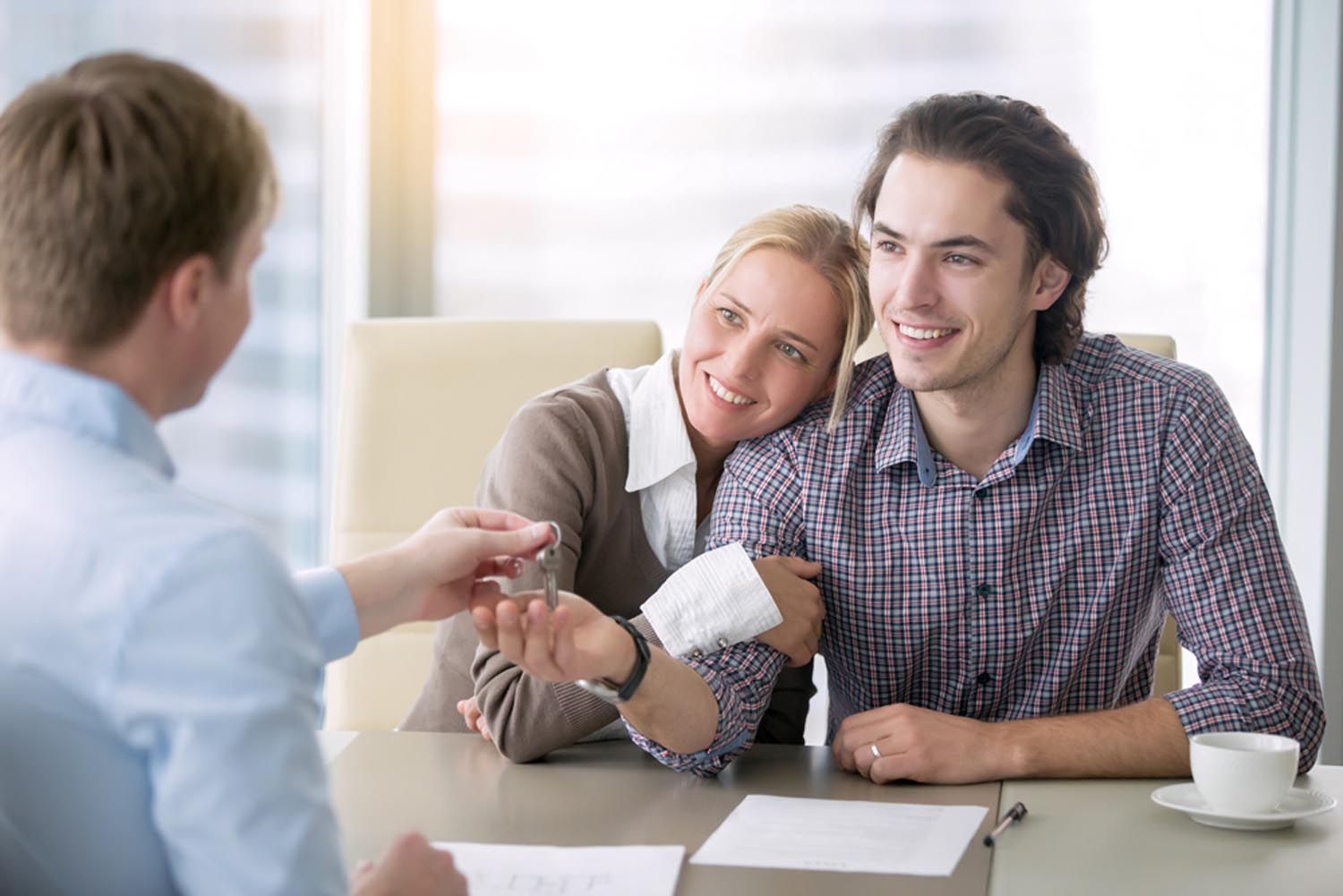 Two people smiling and shaking hands with a man across a desk in a bright office
