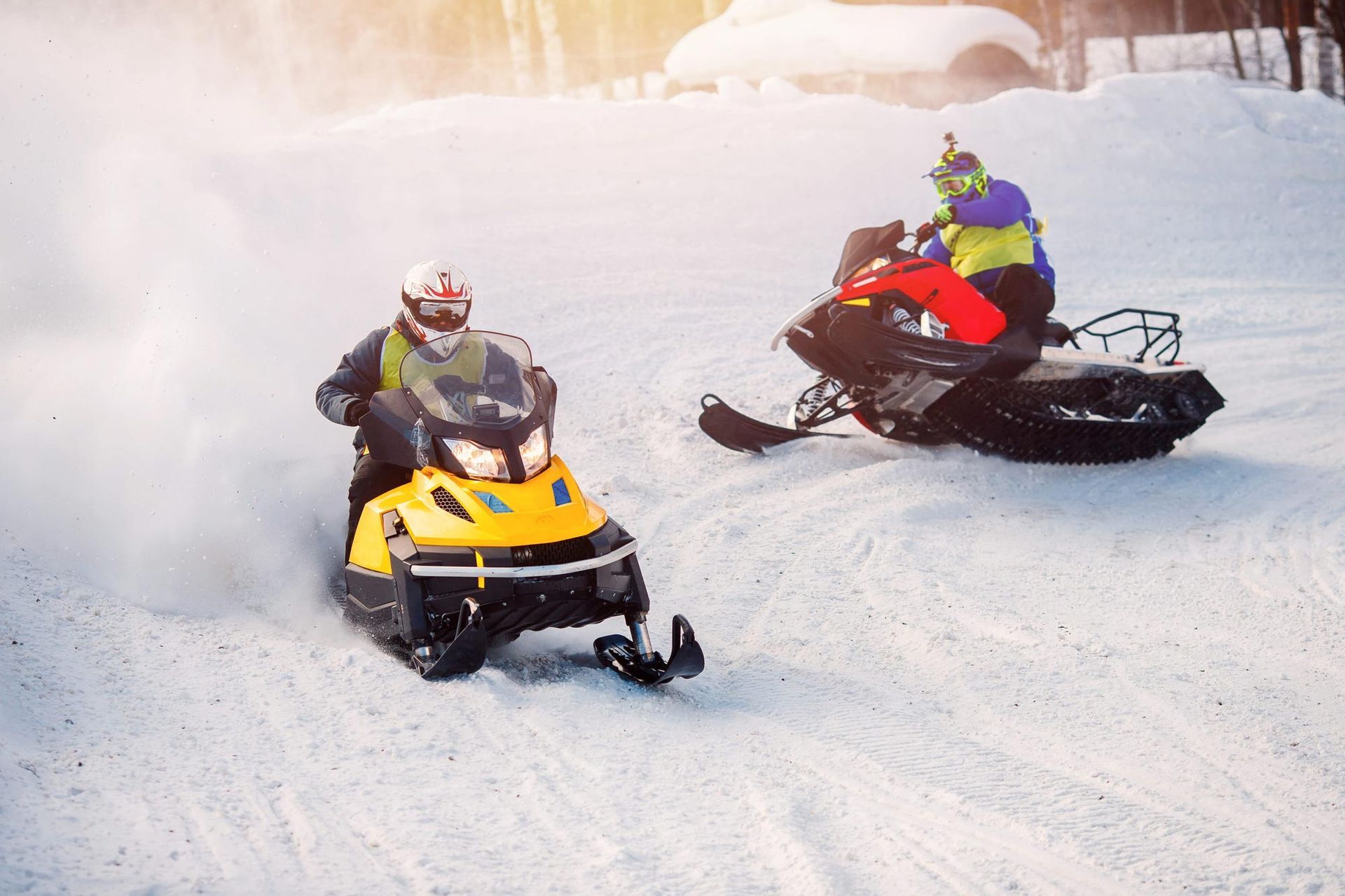 Two snowmobiles racing through fresh snow, one yellow and one red, on a snowy hillside.