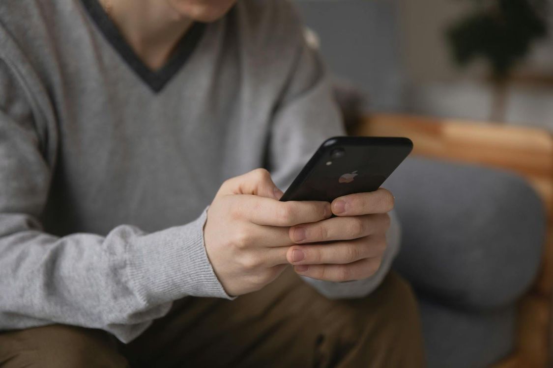 Person in a gray sweater using a smartphone on a couch indoors