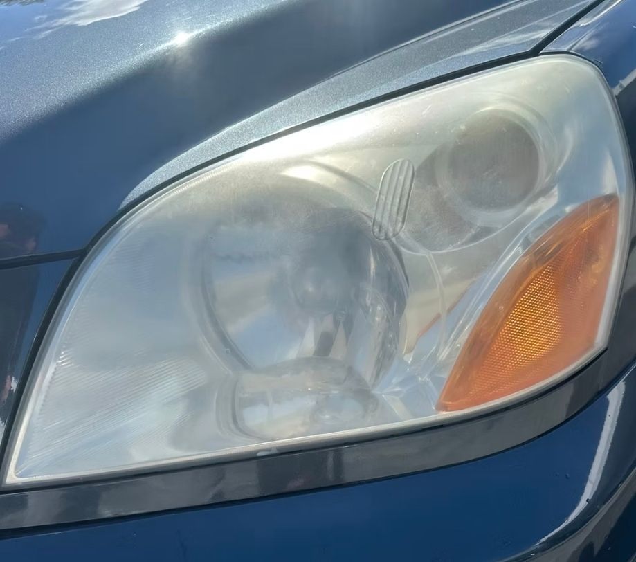 Cloudy car headlight next to a bright orange blinker, on a dark gray car.