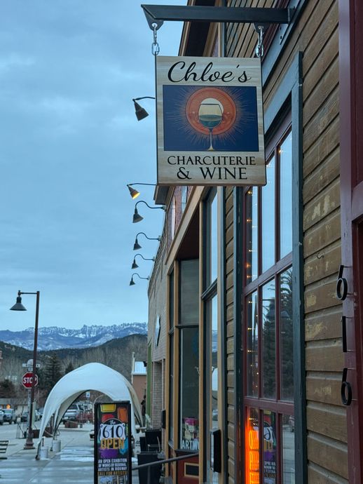 A sign for chloes charcuterie and wine hangs from the side of a building