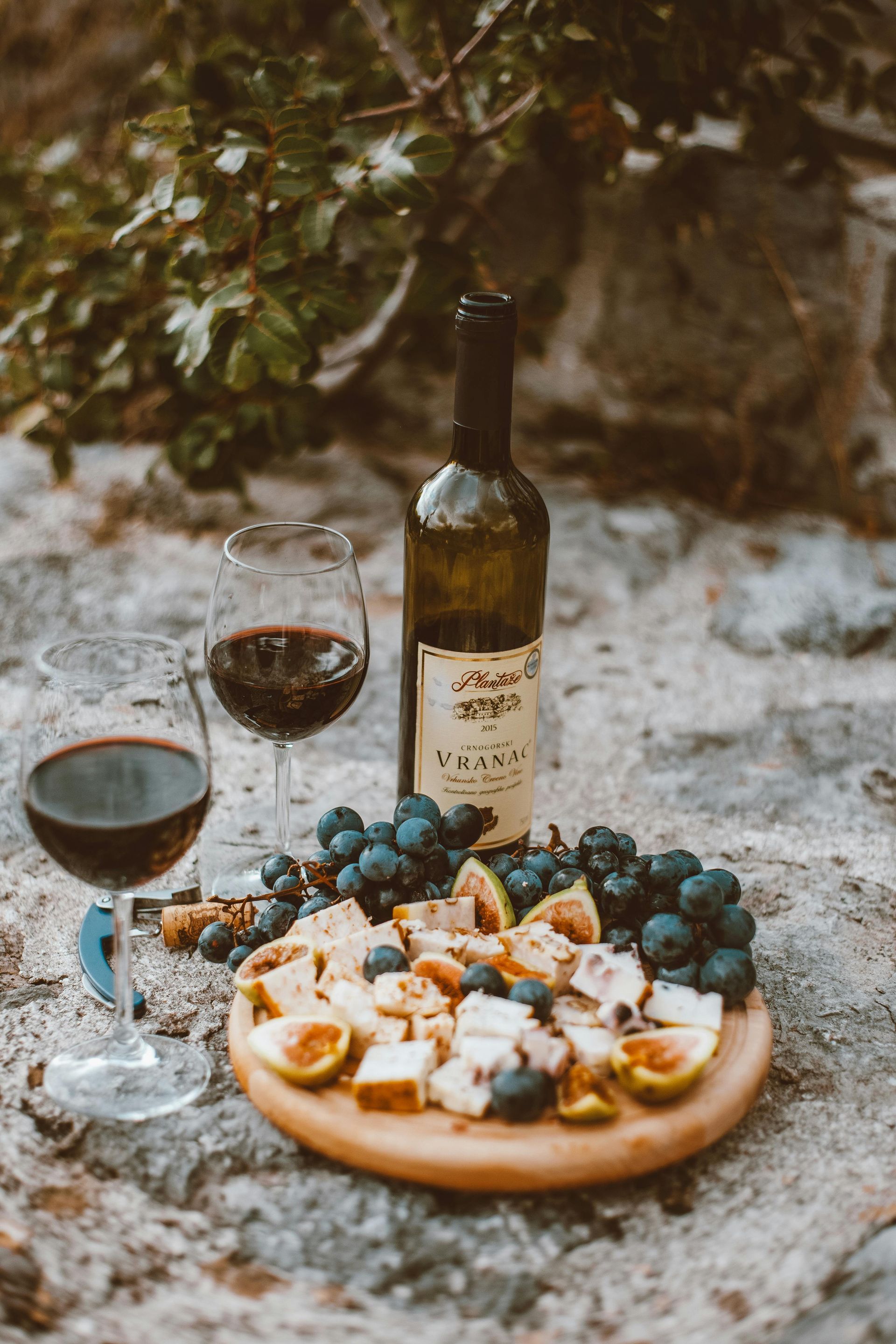 A bottle of wine , two glasses of wine and a plate of food on a rock.