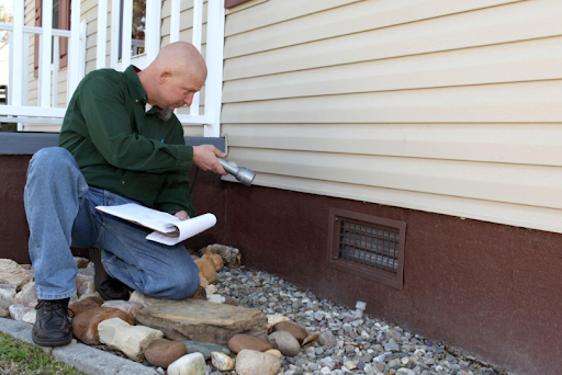 Technician inspecting house siding near the foundation with a notepad and tool
