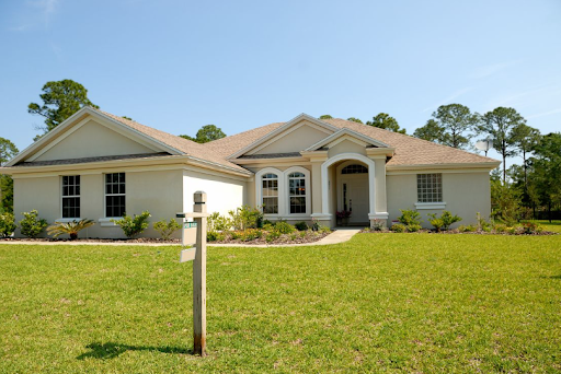 Single-story suburban house with a lawn and white porch columns under a clear blue sky