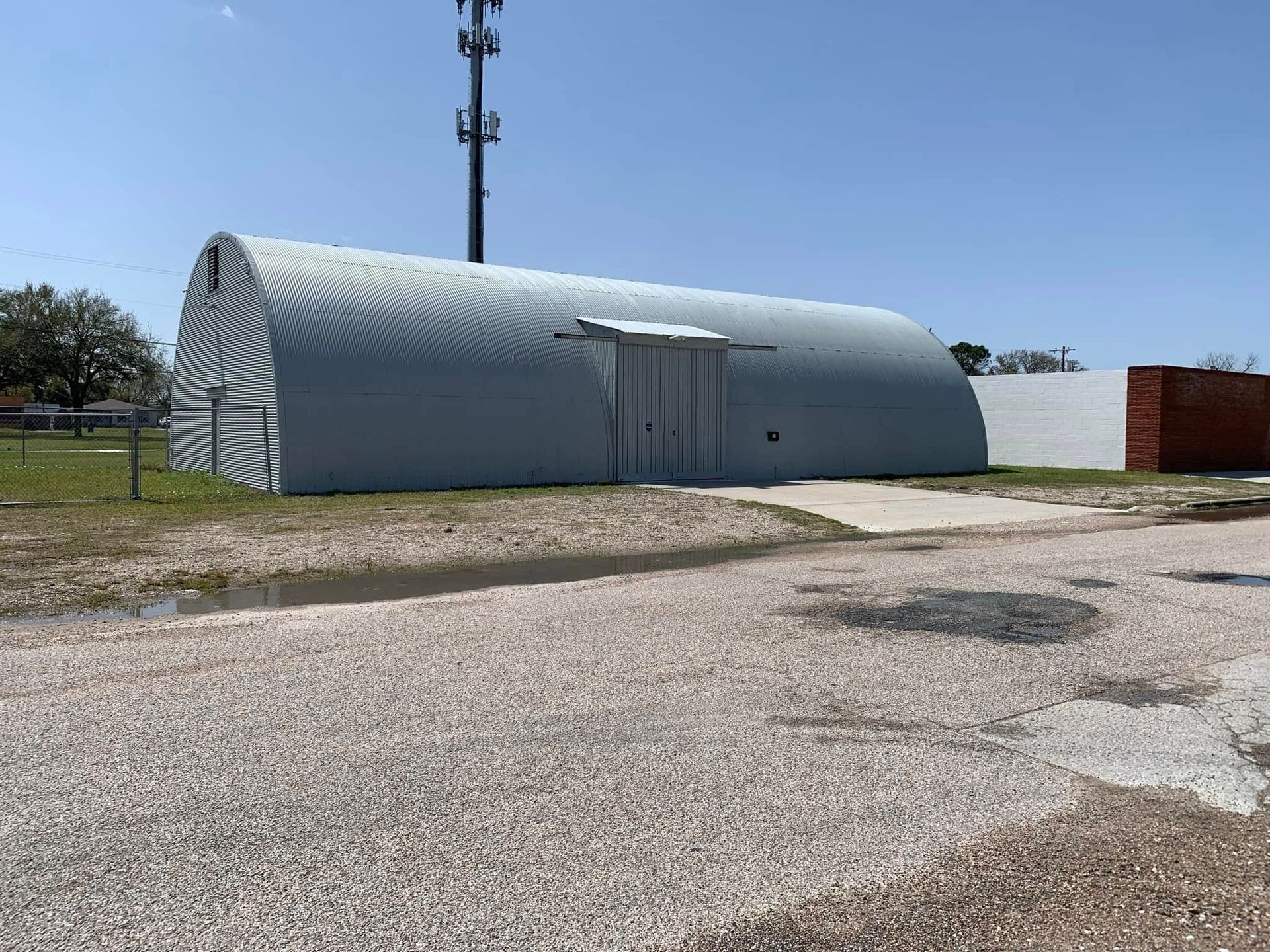 A large gray building is sitting in the middle of a gravel road.
