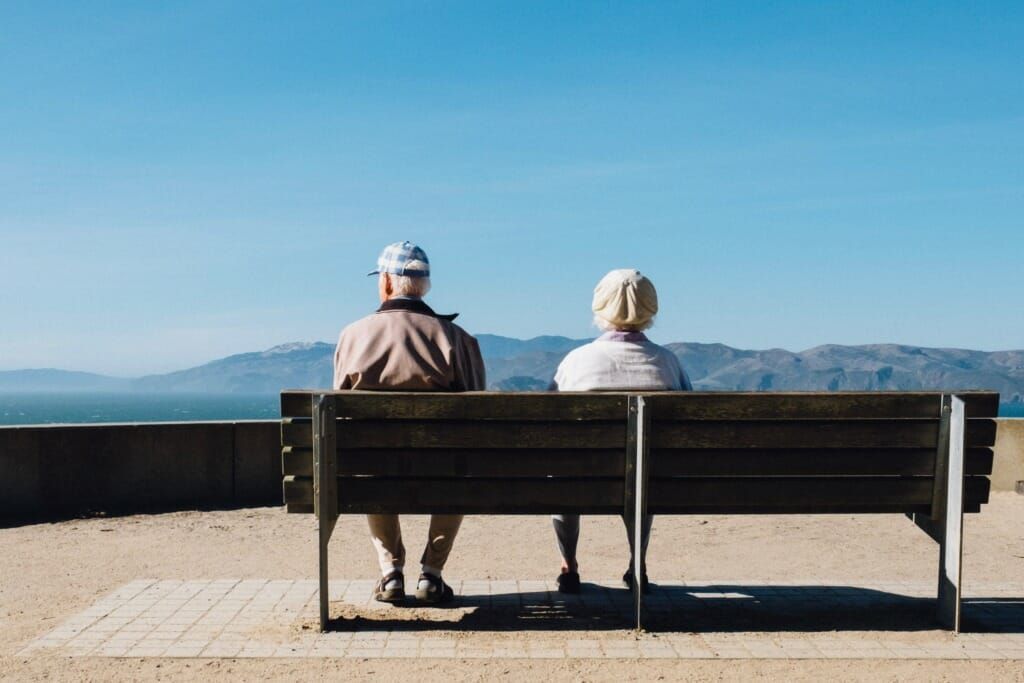Ein Mann und eine Frau sitzen auf einer Bank und blicken auf das Meer.