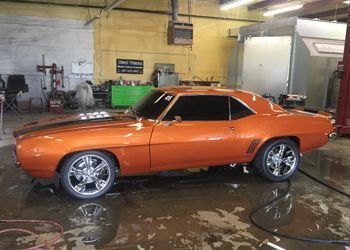 an orange muscle car is parked in a garage .