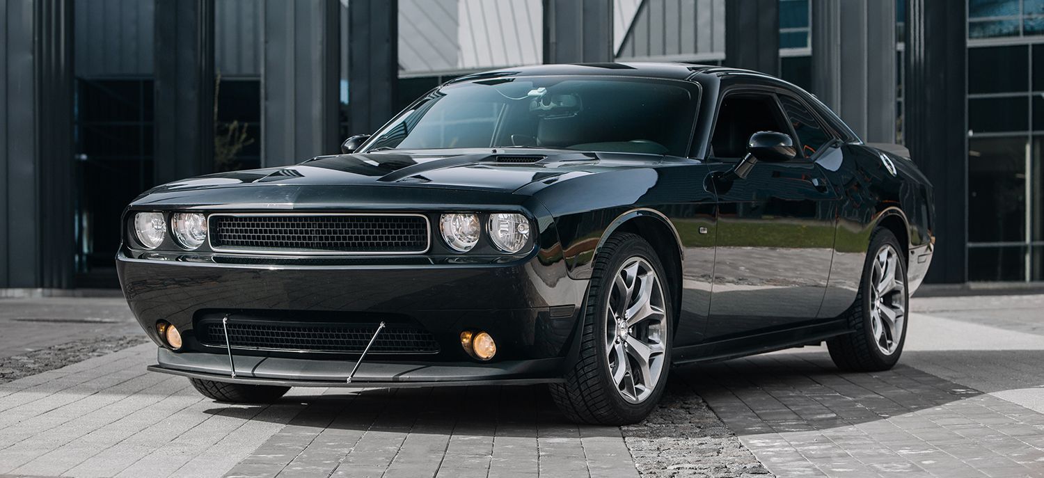 Black Dodge Challenger parked in front of a modern building with a cobblestone driveway.
