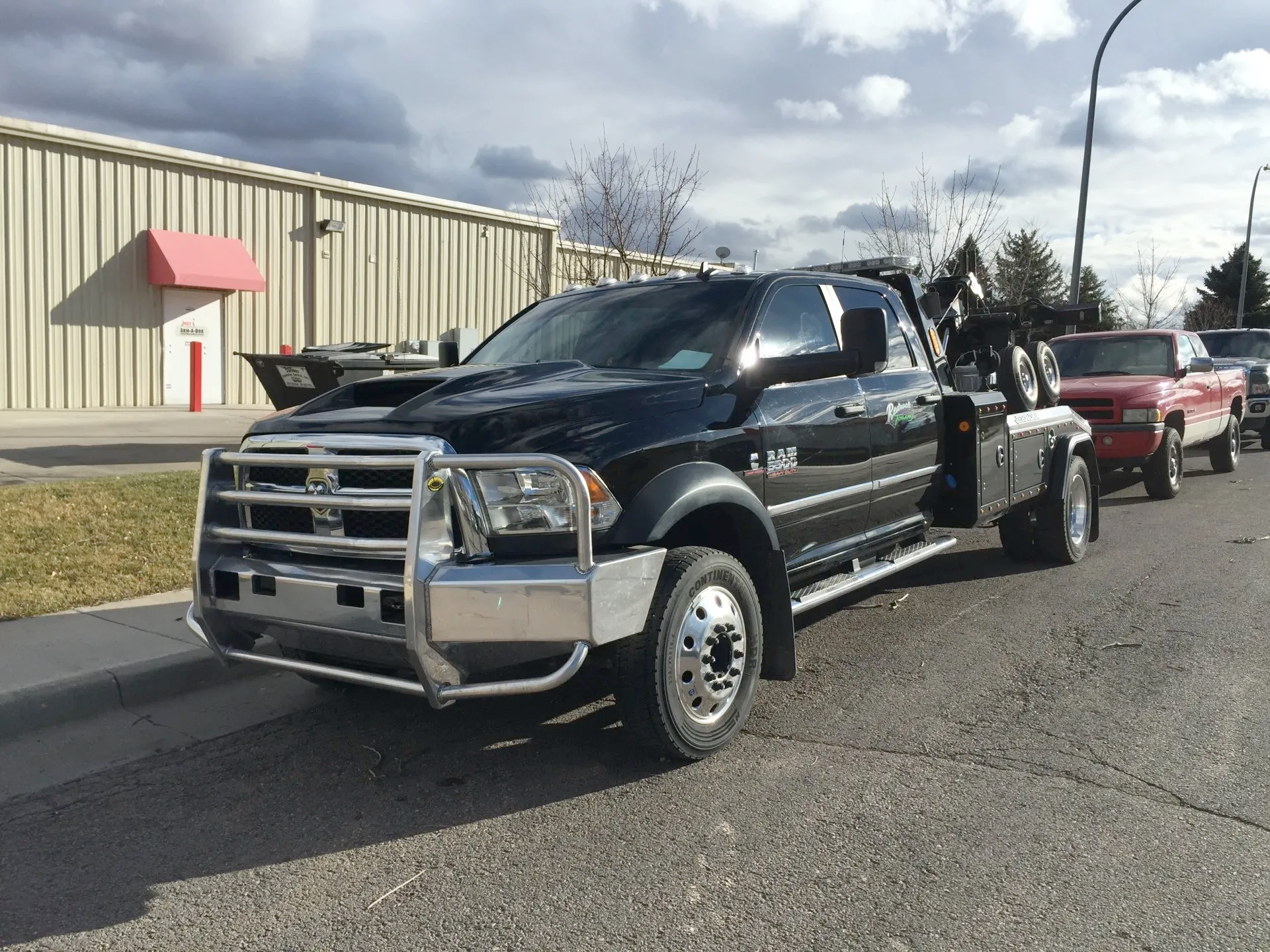 A black tow truck is parked on the side of the road in front of a building.
