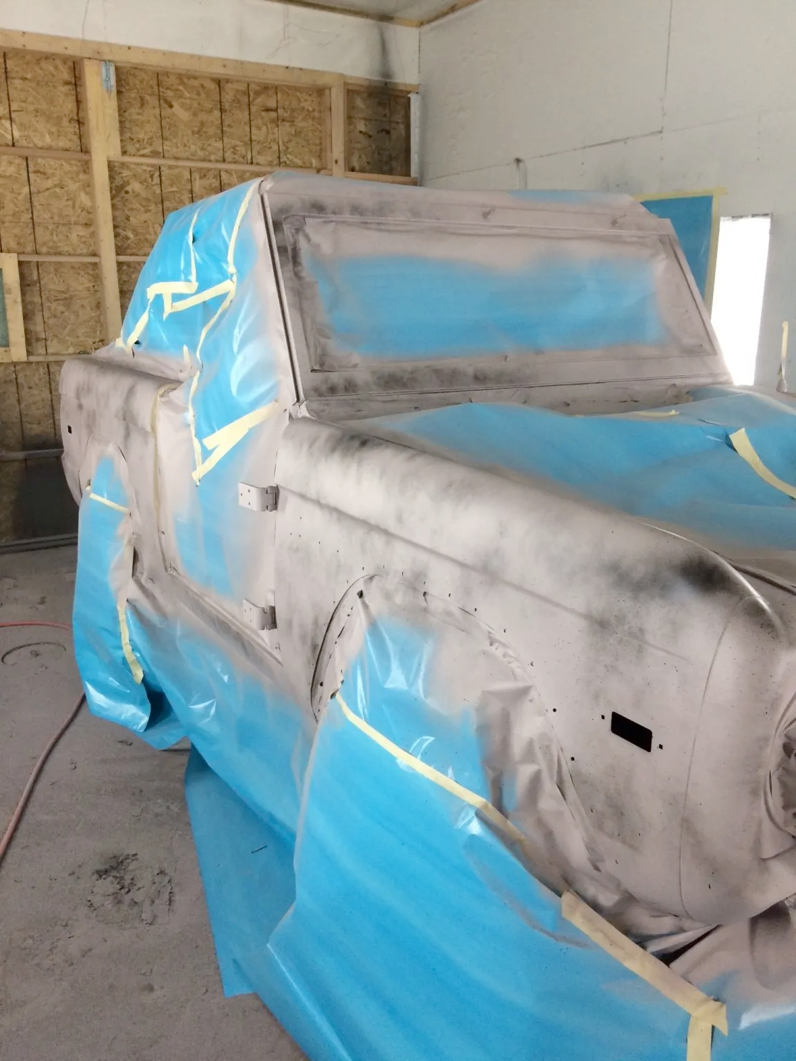 A truck is covered in blue plastic in a garage