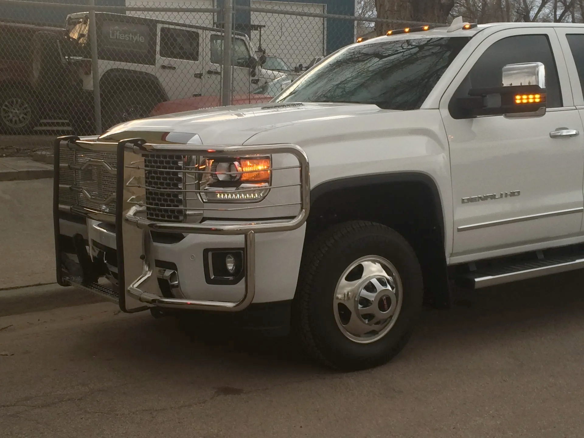 A white truck with a grille is parked on the side of the road.