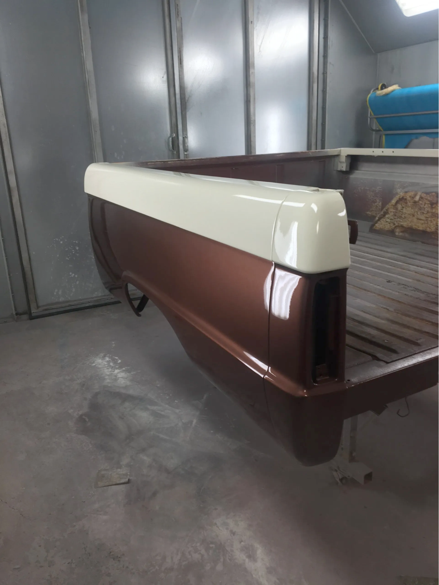 A brown and white truck bed is sitting in a paint booth.