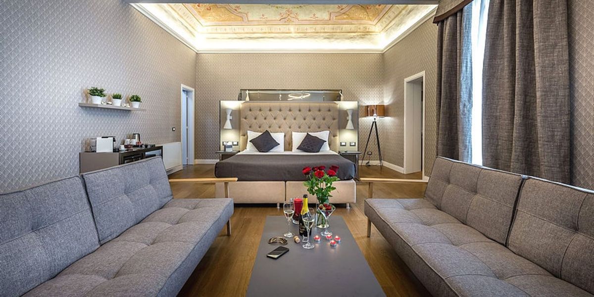 Una suite di lusso con un letto, due divani e un tavolino con fiori e bevande. Le pareti sono decorate con un motivo testurizzato.