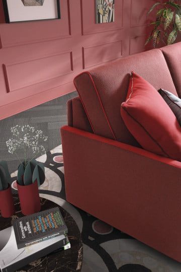 Divano rosso contro una parete dipinta di rosso con pannelli decorativi. Un tappeto a fantasia, piante in vaso e libri completano la scena.
