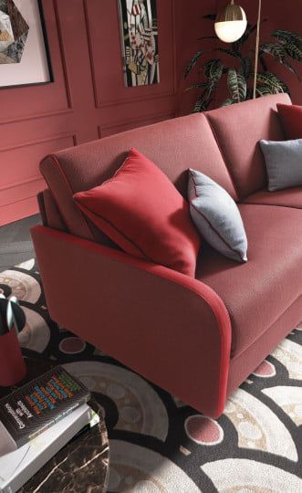 Divano rosso con cuscini decorativi in una stanza con pareti rosse e un tappeto a fantasia.