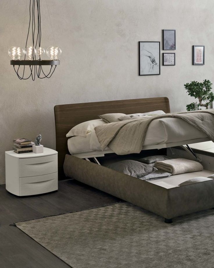 Camera da letto con letto dotato di vano contenitore sollevabile, testiera in legno, comodino e opere d'arte astratte alla parete.