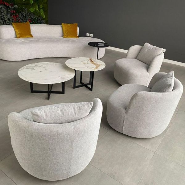 Set di mobili per soggiorno composto da un divano bianco curvo, due poltrone circolari e un paio di tavolini da caffè con piano in marmo.