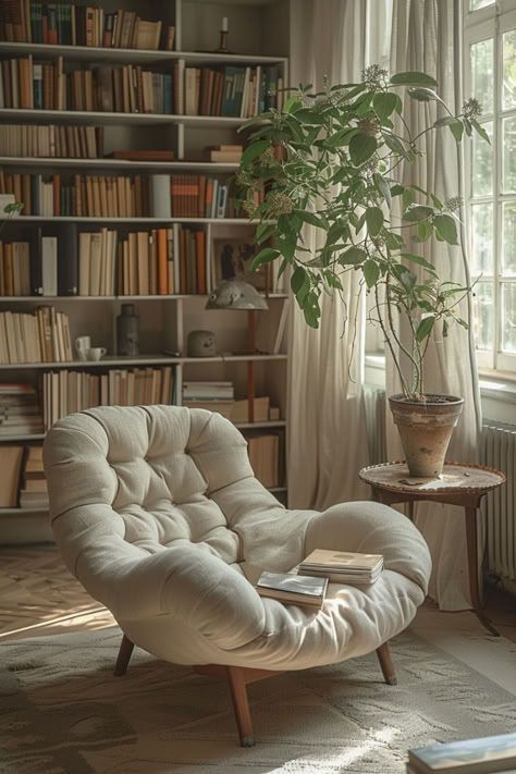 Accogliente angolo lettura: poltrona imbottita color crema, librerie, luce solare, pianta in vaso, libri sul tavolo e una finestra.