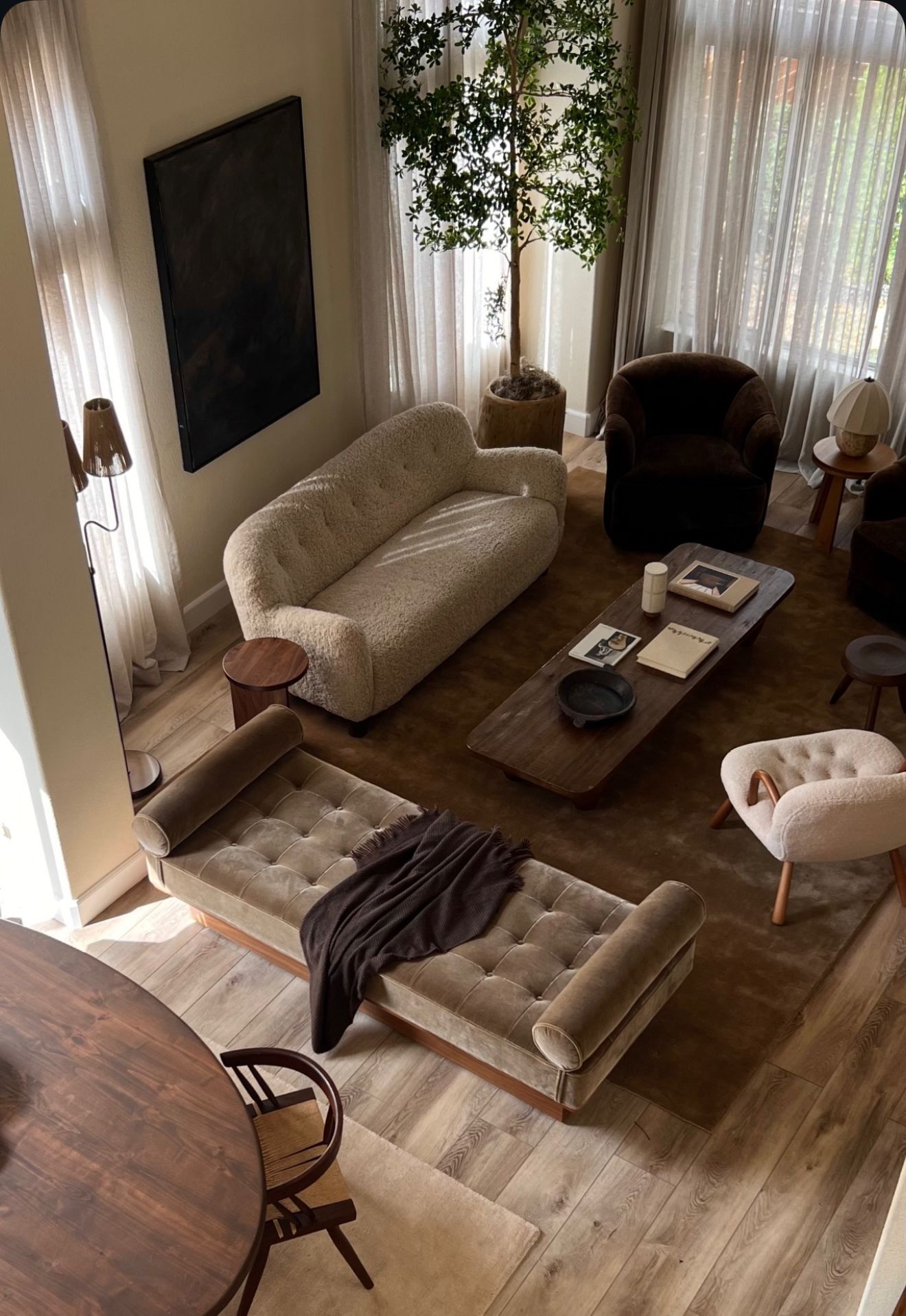 Vista dall'alto di un soggiorno dai toni neutri. L'arredamento include un divano capitonné, un tavolino da caffè e una seduta vicino a un albero.