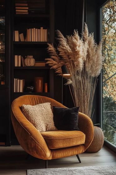 Accogliente angolo lettura: sedia curva giallo senape con cuscini, erba alta della pampa e una libreria vicino a una finestra con vista sul fogliame autunnale.