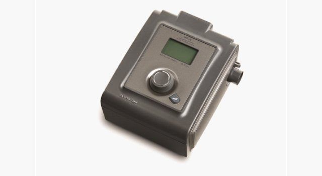 CPAP machine, gray, with a screen, dial, and hose connection on the side.
