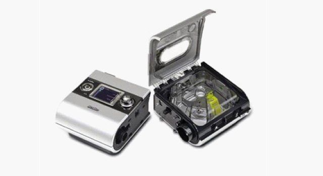 CPAP machine with open humidifier chamber, and top. Silver and black.