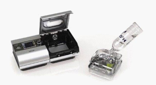 Silver CPAP machine with open water chamber being filled with water.