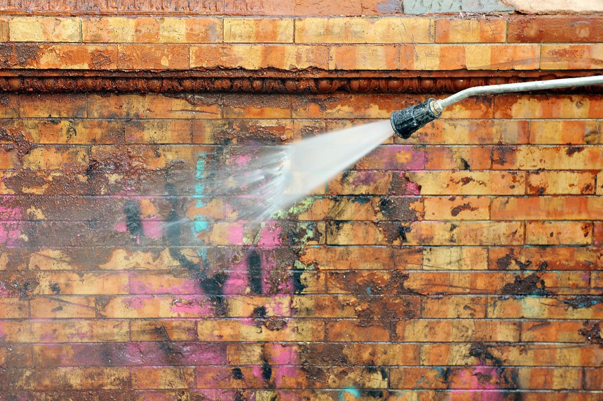 A person is cleaning a brick wall with a high pressure washer.