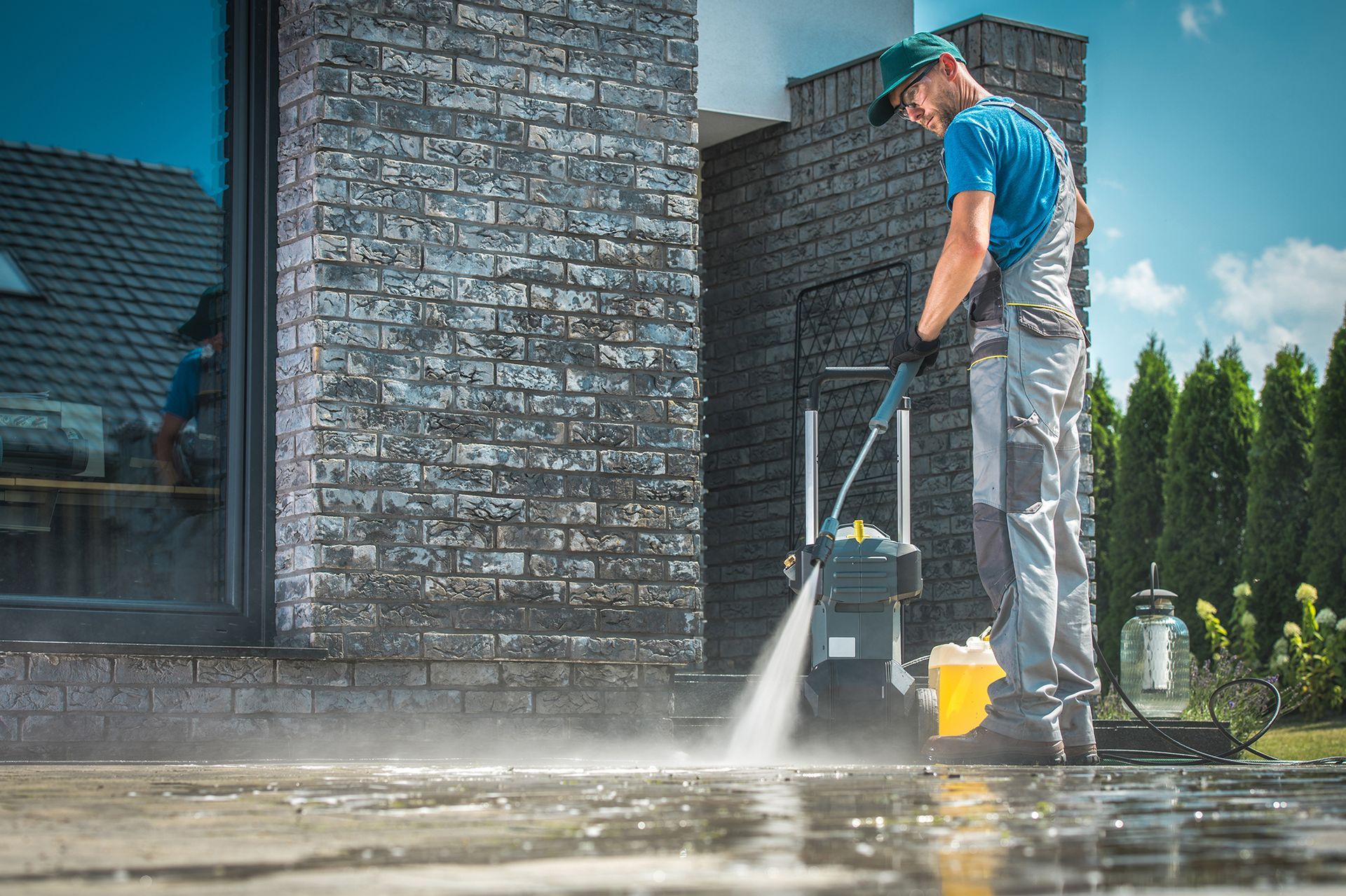 A man is using a high pressure washer to clean the sidewalk in front of a brick building.