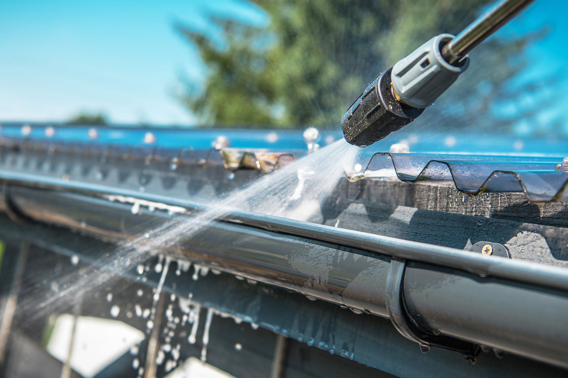 A person is cleaning a gutter with a high pressure washer.