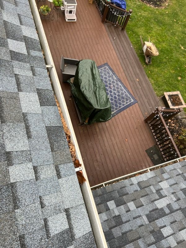 Overhead view of a roof with a gutter filled with debris, leading to a deck with covered furniture.