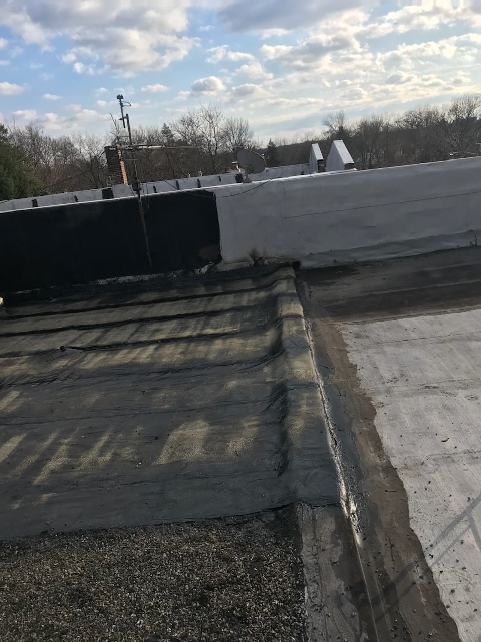 View of a weathered flat roof with dark and light sections, a cloudy sky in the background.