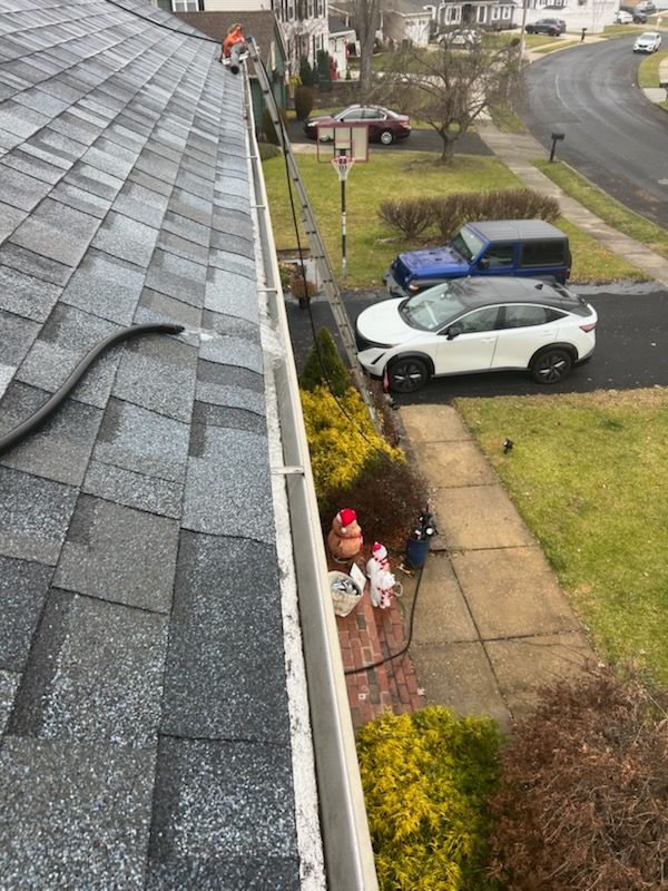 A roof with a gutter, a garden, a sidewalk, and cars parked on a residential street.