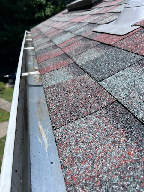 Close-up of a roof with red, gray, and black shingles, and a metal gutter along the edge.