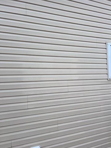 Tan horizontal siding on a house with a window visible on the right side.