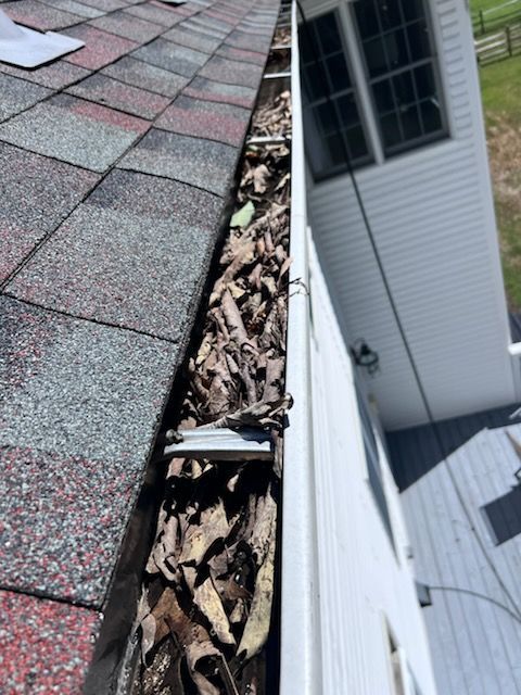 Gutter filled with brown leaves next to a red roof and white house siding.