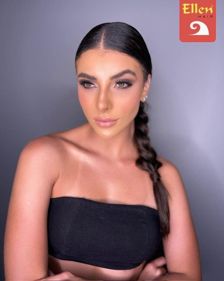 Mulher com cabelo penteado para trás em uma trança, usando um top preto tomara que caia, olhando para o lado com fundo cinza.