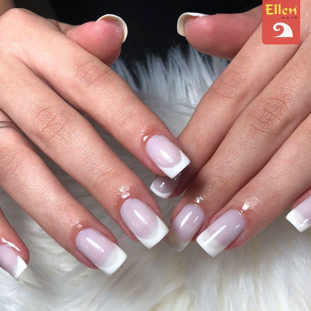 Manicure francesa em mãos de pele clara, com pontas brancas quadradas sobre esmalte transparente.
