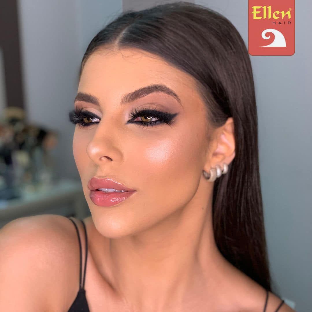 Mulher com maquiagem esfumada nos olhos, lábios brilhantes e brincos de argola prateados. O fundo está desfocado.